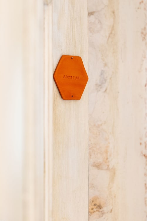 Orange hexagonal room key tag with 'ADMETTAR' text on light wood door at Mas Bella Cortis B&B in La Garde-Adhémar, France