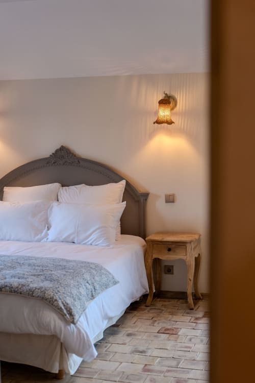 Elegant bedroom at Mas Bella Cortis with ornate headboard, white bedding, wooden nightstand, and brass wall sconce in La