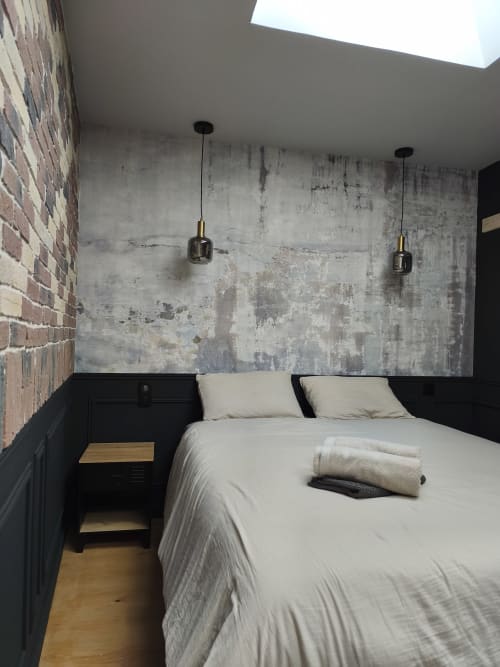 Chambre Hippo à la mezzanine d'Escale à Clisson : mur en béton brut, luminaires suspendus et lit à cadre noir avec literie crème.