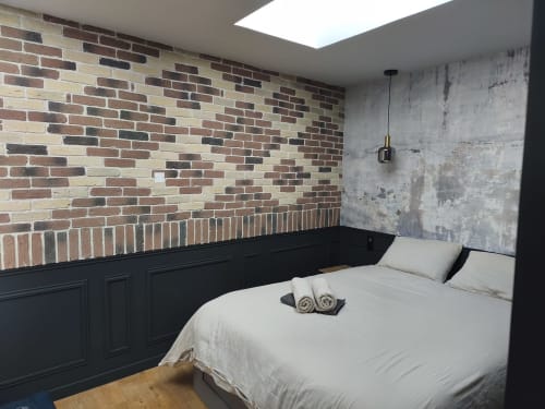 Chambre loft moderne à Clisson avec murs en briques apparentes, panneaux noirs, literie blanche et puits de lumière