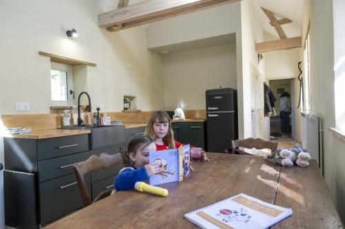 Deux enfants dans la cuisine de la maison d'hôtes Le Colombier à la Cour Du Liège, Baugé-en-Anjou, avec électroménagers noirs modernes et salle à manger en bois