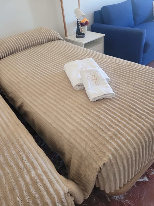 Dormitorio de apartamento frente al mar en Apartamentos A la Orilla del Mar con ropa de cama a rayas beige, toallas blancas y sofá azul