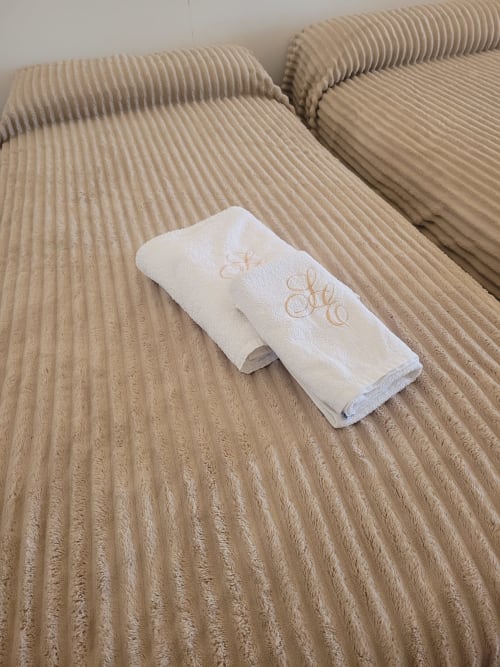 Toallas blancas con iniciales bordadas sobre colcha acanalada beige en apartamento de Matalascañas