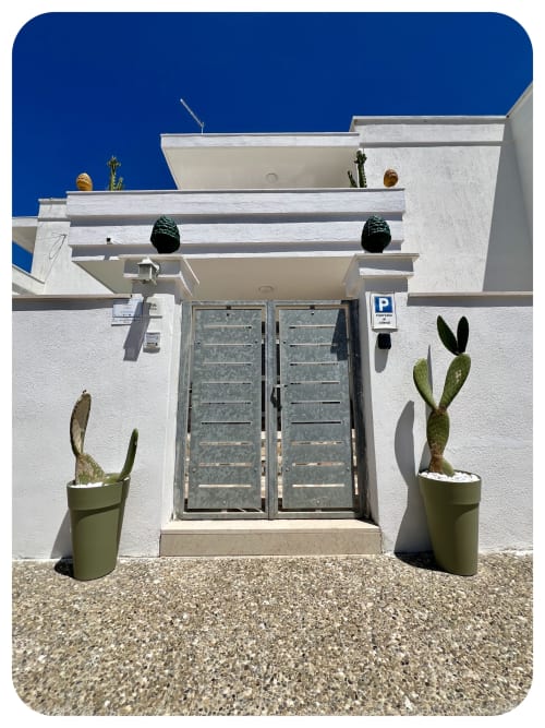 Modern white villa entrance in Ostuni with double doors, potted cacti, and vibrant blue sky