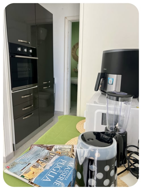 Modern kitchen area in Villa Adua at Dimore Adua, Ostuni, with black cabinetry, coffee machine, and green garden view door