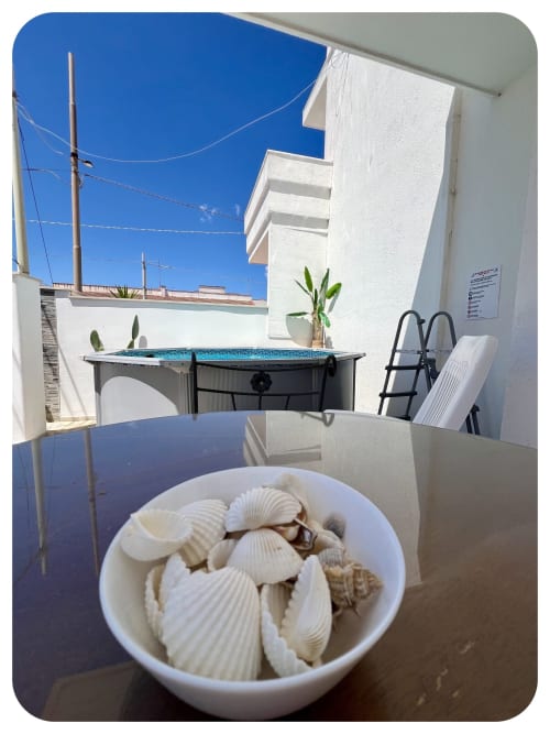 White seashells in bowl on terrace at Dimore Adua villa, Ostuni, with garden view and pool