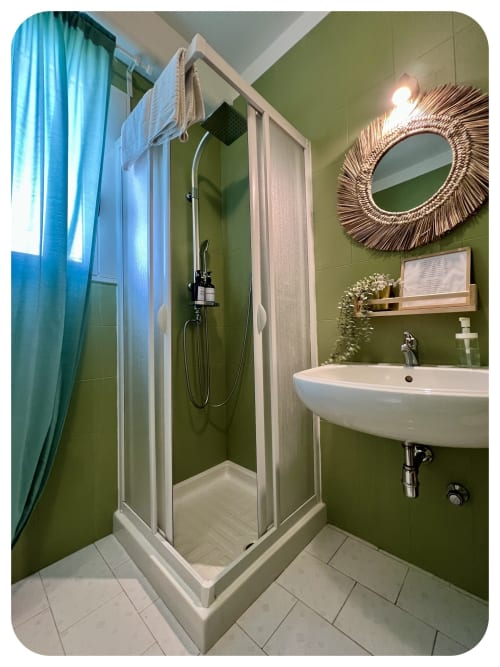 Modern bathroom at Villa Adua in Ostuni with olive green walls, white sink, shower enclosure, and decorative mirror