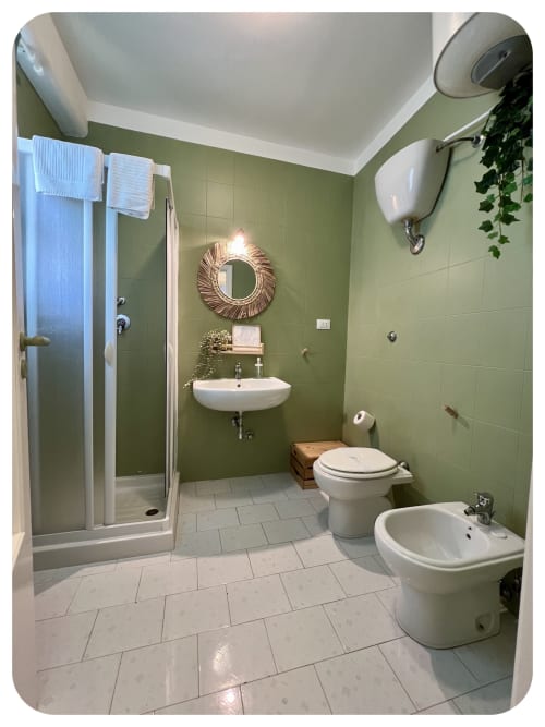 Modern bathroom at Villa Adua in Ostuni with sage green walls, white fixtures, rainfall showerhead, and decorative mirror