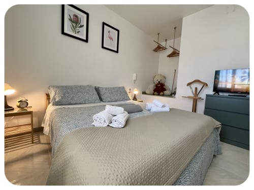 Modern bedroom at Dimore Adua villa in Ostuni with gray quilted bedding, framed artwork, TV, and white towels