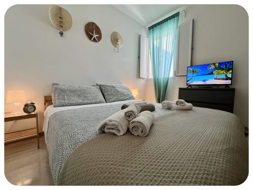 Villa Adua bedroom in Ostuni with queen bed, rolled towels, wall art, TV, turquoise curtains, and garden view