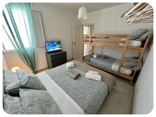 Spacious bedroom at Villa Adua, Ostuni, with bunk beds, single bed, TV, and garden view through turquoise curtains