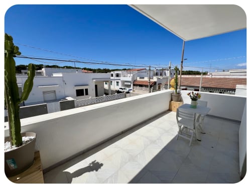 Sunny rooftop terrace at Villa Adua in Ostuni with white loungers, potted cactus, and garden views