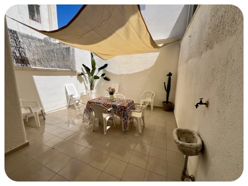 Outdoor patio at Villa Adua in Ostuni with shaded seating area, dining table, white chairs, and Mediterranean decor under