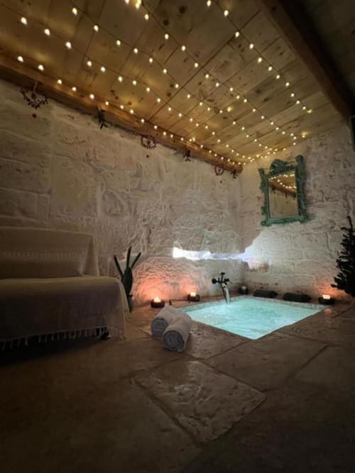 Lussuoso bagno spa di Dimore Adua con vasca idromassaggio, luci decorative, candele e muri in pietra bianca a Ostuni