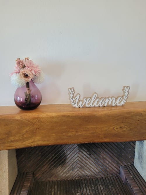 Letrero de bienvenida y jarrón con flores rosas en repisa de madera en apartamento de Matalascañas con decoración de vista al mar