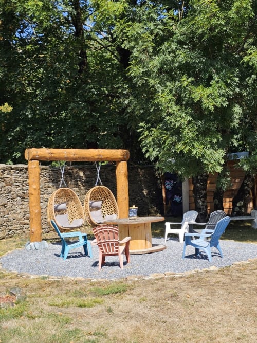 Espace de détente en plein air à la Bastide du Thoré avec fauteuils suspendus, chaises Adirondack et verdure luxuriante à Labastide-Rouairoux
