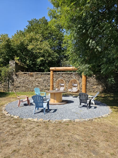 Espace de détente extérieur à la Bastide du Thoré avec chaises Adirondack, balançelles suspendues et mur en pierre à Labastide-Rouairoux