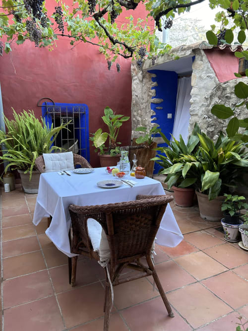 Intimate courtyard dining setup at Casa Gallinera with white-draped table, wicker chairs, and vibrant pink walls in Alicante