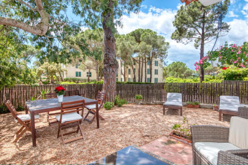 Terrasse extérieure de Finques Garcia Enrich à Palafrugell avec mobilier en bois, grands arbres et fleurs roses