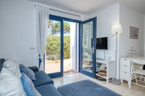 Chambre lumineuse aux portes bleues donnant sur le jardin, canapé bleu et mobilier blanc chez Finques Garcia Enrich à Palafrugell