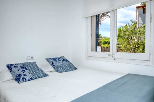 Chambre lumineuse aux Finques Garcia Enrich à Palafrugell avec coussins à motifs bleus, literie blanche et grandes fenêtres