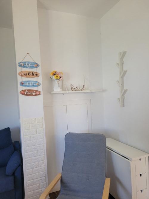 Dormitorio luminoso con decoración costera, estantería blanca, silla azul y colgante temático marino en Apartamentos A la