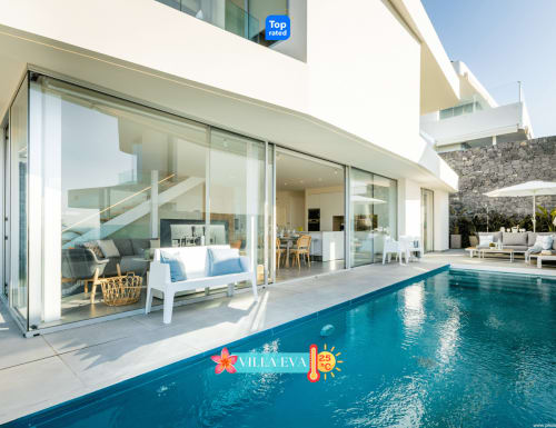 Terraza con piscina climatizada de Villa Eva con vistas al mar, Adeje. Arquitectura moderna, puertas de cristal, zona de descanso y comedor