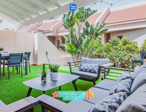 Casa adosada con terraza al atardecer en Adeje: césped artificial, zona de descanso, mesa de comedor, plantas frondosas y vistas al mar