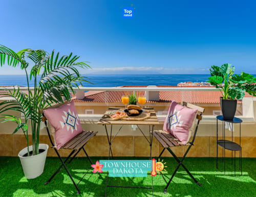 Terraza de casa Dakota con vistas al mar, sillas rosadas tapizadas, mesa servida, plantas en macetas y paisaje costero en Adeje