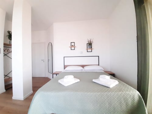 Camera moderna in B&B Bari Centro con letto matrimoniale, cuscini bianchi, coperta verde testurizzata, arredamento minimalista e piante in vaso