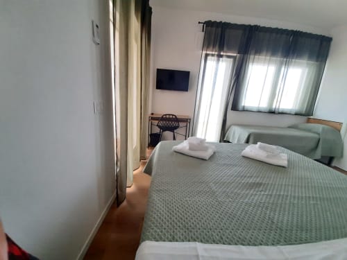 Camera moderna al B&B Bari Centro con letto matrimoniale, TV a schermo piatto, scrivania e vista giardino attraverso tende trasparenti a Bari
