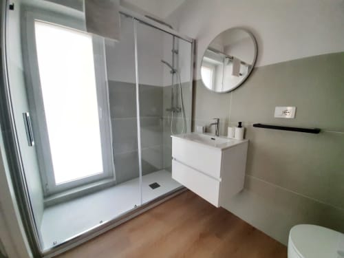 Bagno moderno di B&B Bari Centro con vanity bianca, specchio rotondo, doccia walk-in, parete accent verde e pavimentazione in legno