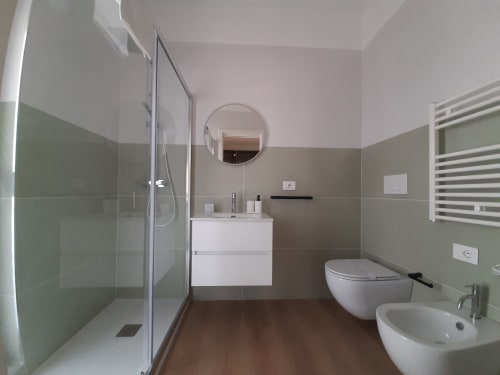 Bagno moderno nel B&B di Bari con doccia aperta, lavabo bianco, wc, bidet, specchio rotondo, scaldasalviette e legno