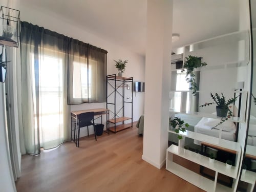 Camera moderna in hotel a Bari con zona lavoro, letto in soppalco, pavimenti in legno e vista sulla città attraverso tende trasparenti