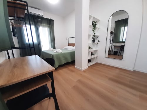 Camera da letto moderna a Bari con scrivania in legno, letto verde, specchio ad arco, scaffali e luce naturale dalle finestre