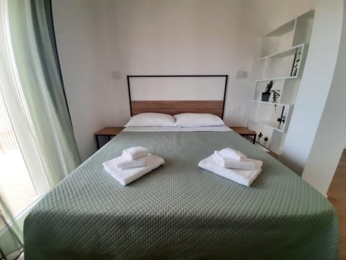 Camera da letto moderna a Bari con letto queen size, cuscini bianchi, coperta verde, testata in legno e mensole con pianta in vaso