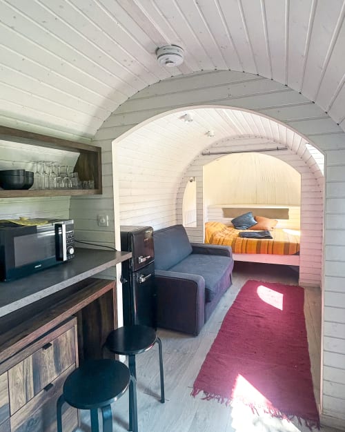 Intérieur cozy d'une tiny house à la Cour Du Liège : cuisine, coin salon et chambre visibles par une porte voûtée