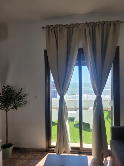Apartamento frente al mar con terraza vista al océano, cortinas translúcidas enmarcando puertas de cristal con vista a jardín verde y océano