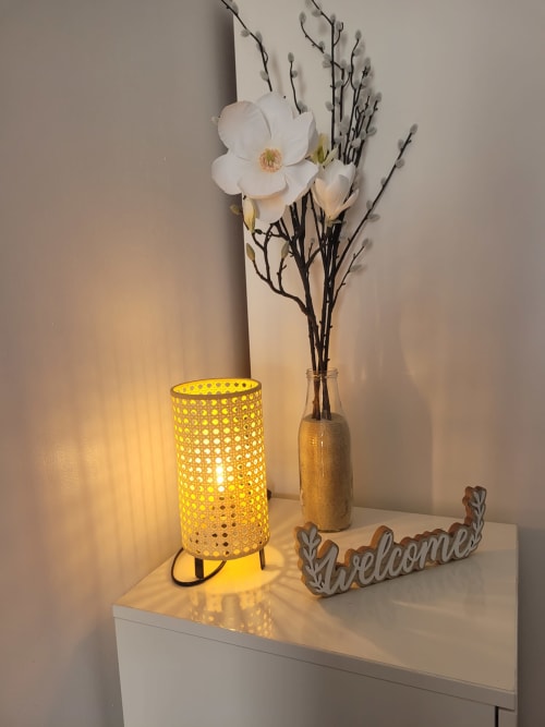 Mesilla de noche decorada con lámpara amarilla, flores blancas y cartel de bienvenida en apartamento de Matalascañas