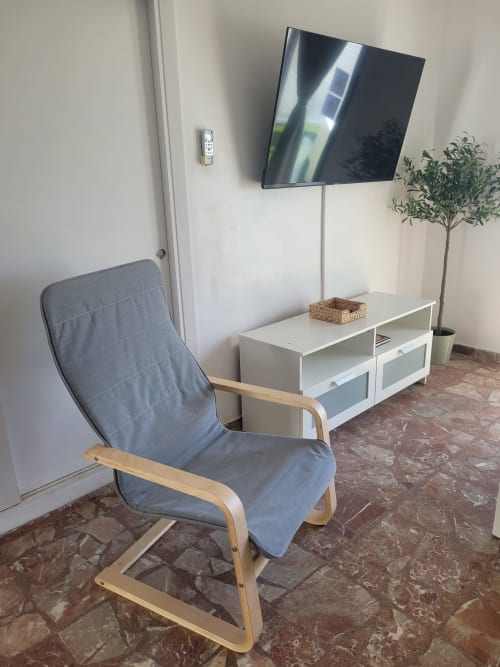 Moderno salón de hotel Matalascañas con sillón azul, televisor montado en pared, mueble blanco y planta decorativa