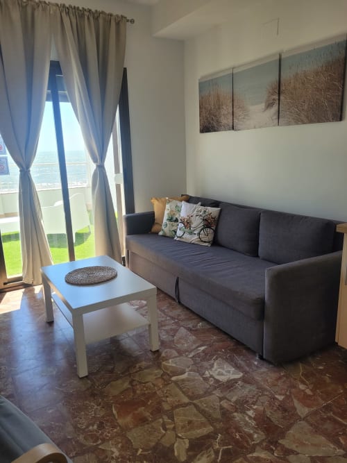 Sala de estar de estudio moderno con sofá gris, mesa de café blanca y vistas al mar a través de ventanales