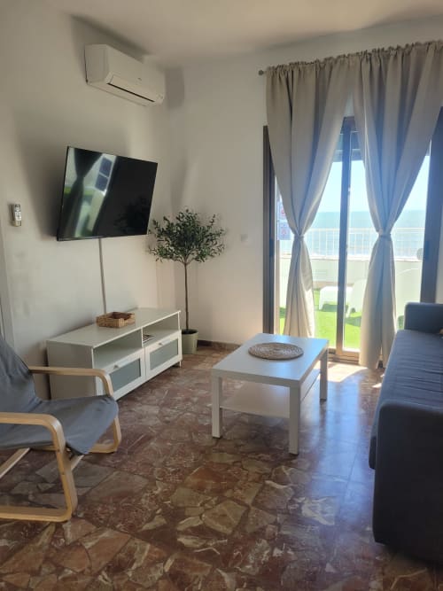 Moderno salón con vistas al mar, televisión, cómodos asientos y acceso a la terraza en Apartamentos A la Orilla del Mar