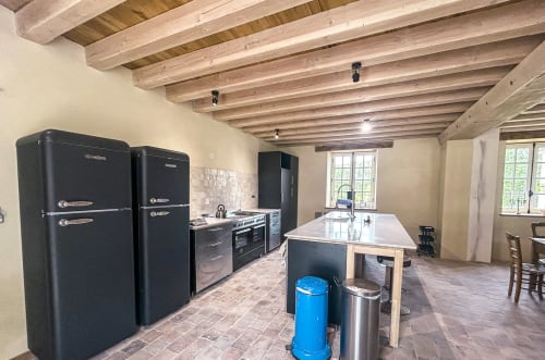 Grande cuisine spacieuse à la Cour Du Liège avec appareils rétro noirs, poutres en bois et coin repas à Baugé-en-Anjou