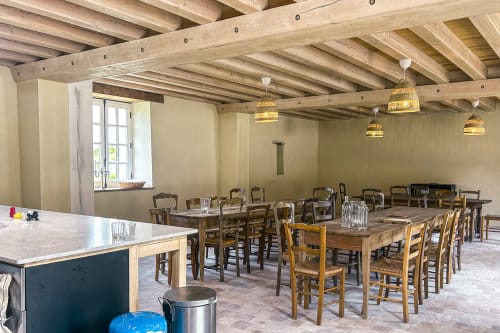 Salle à manger spacieuse à la Cour Du Liège avec poutres en bois, chaises rustiques, tables, luminaires suspendus et vues sur le jardin