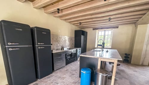 Cuisine moderne avec appareils rétro noirs, îlot central et poutres apparentes à Cour Du Liège, Baugé-en-Anjou