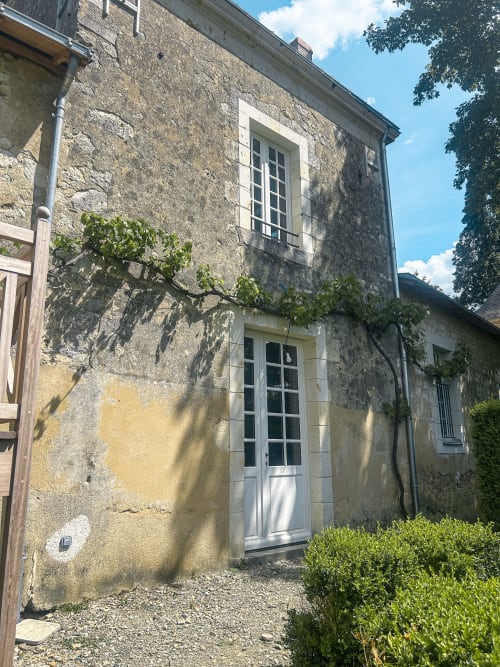 Façade de maison en pierre à la Cour Du Liège avec porte blanche, lierre et jardin à Baugé-en-Anjou