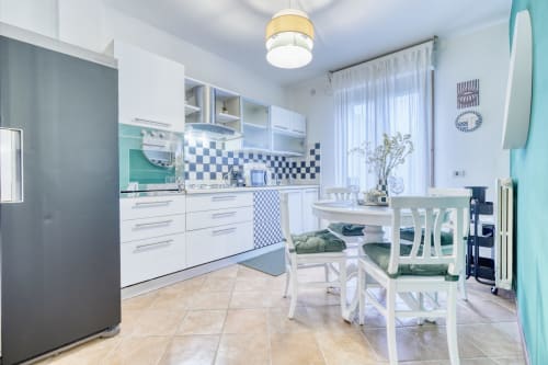 Cucina moderna bianca con accenti turchesi, schienale a scacchi, zona pranzo con sedie bianche in lussuoso appartamento B&B