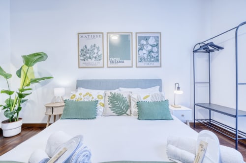 Camera da letto moderna e luminosa nella lussuosa B&B di Pisa con testata blu, piante tropicali, cuscini stratificati, opere d'arte e attaccapanni in metallo