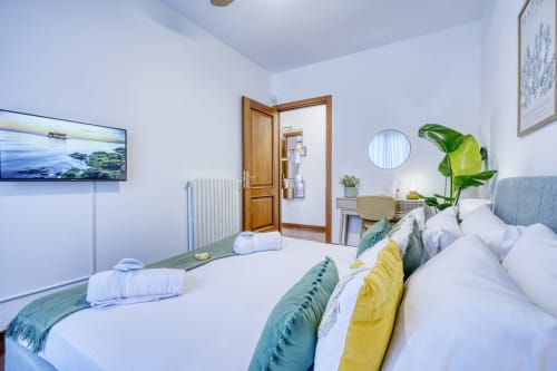 Camera da letto moderna presso SleepWithMe Luxury B&B a Pisa con biancheria bianca, dettagli verdi, TV a schermo piatto e vista sul giardino