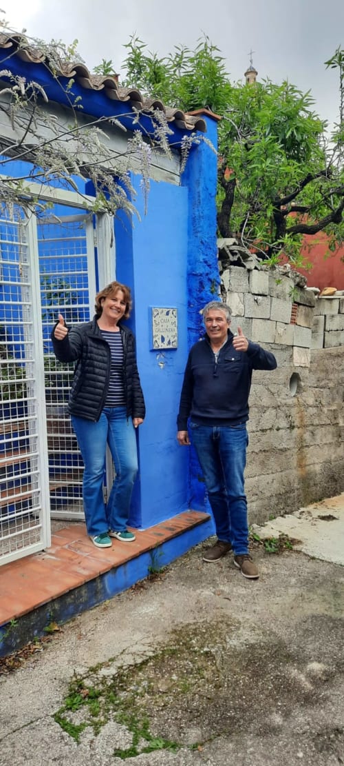 Deux clients donnant un pouce levé devant l'entrée bleue de la gîte rural Casa Gallinera à Alicante